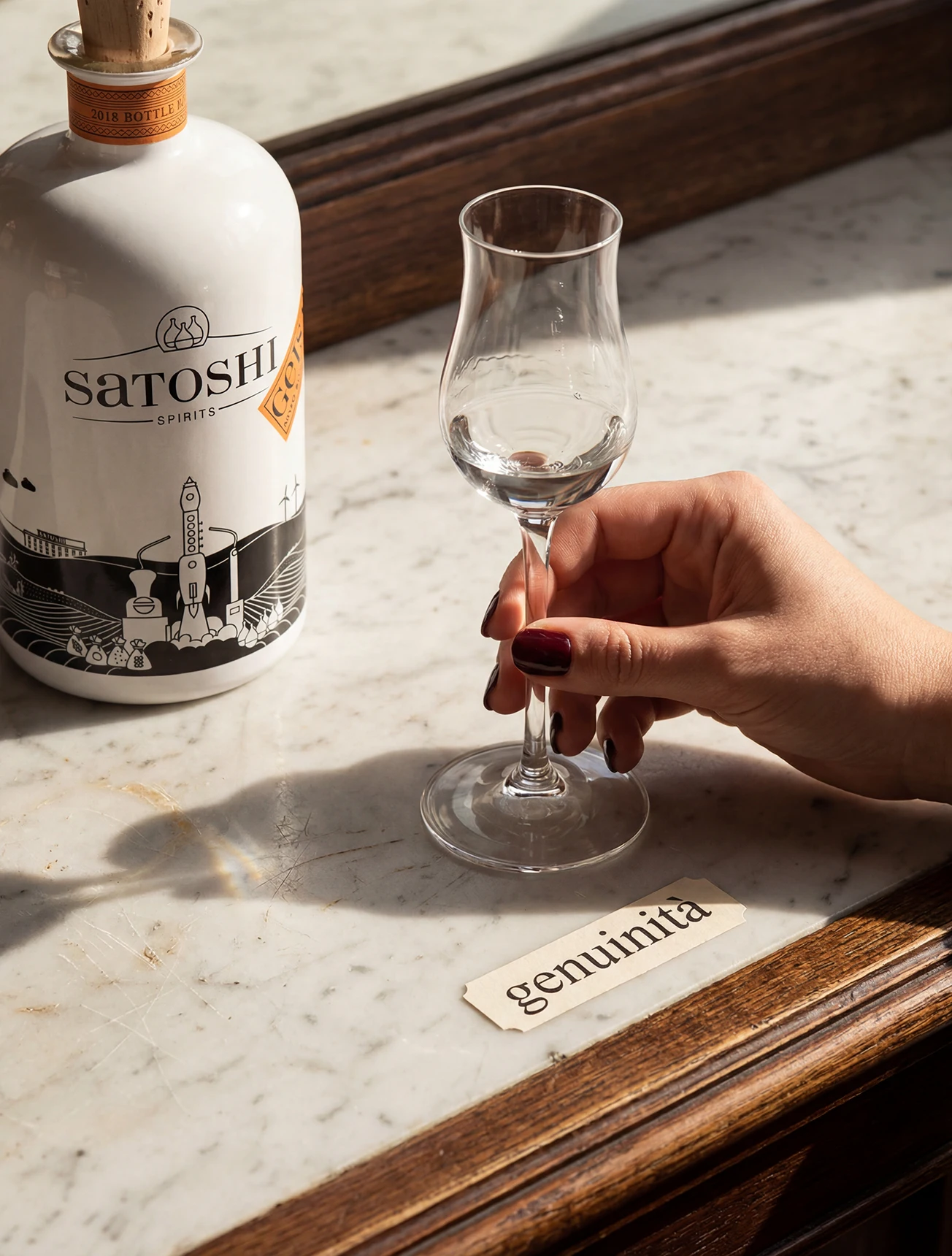 Obstbrandglas mit klarem Destillat neben einer Flasche Satoshi Blutorangengeist