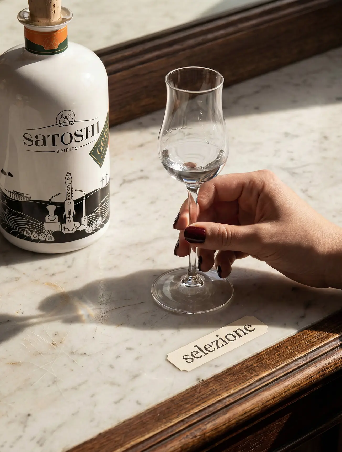 Satoshi Bitterorangendestillat auf einem Bar Tresen neben einem Obstbrandglas, das von einer einer Frauenhand gegriffen wird